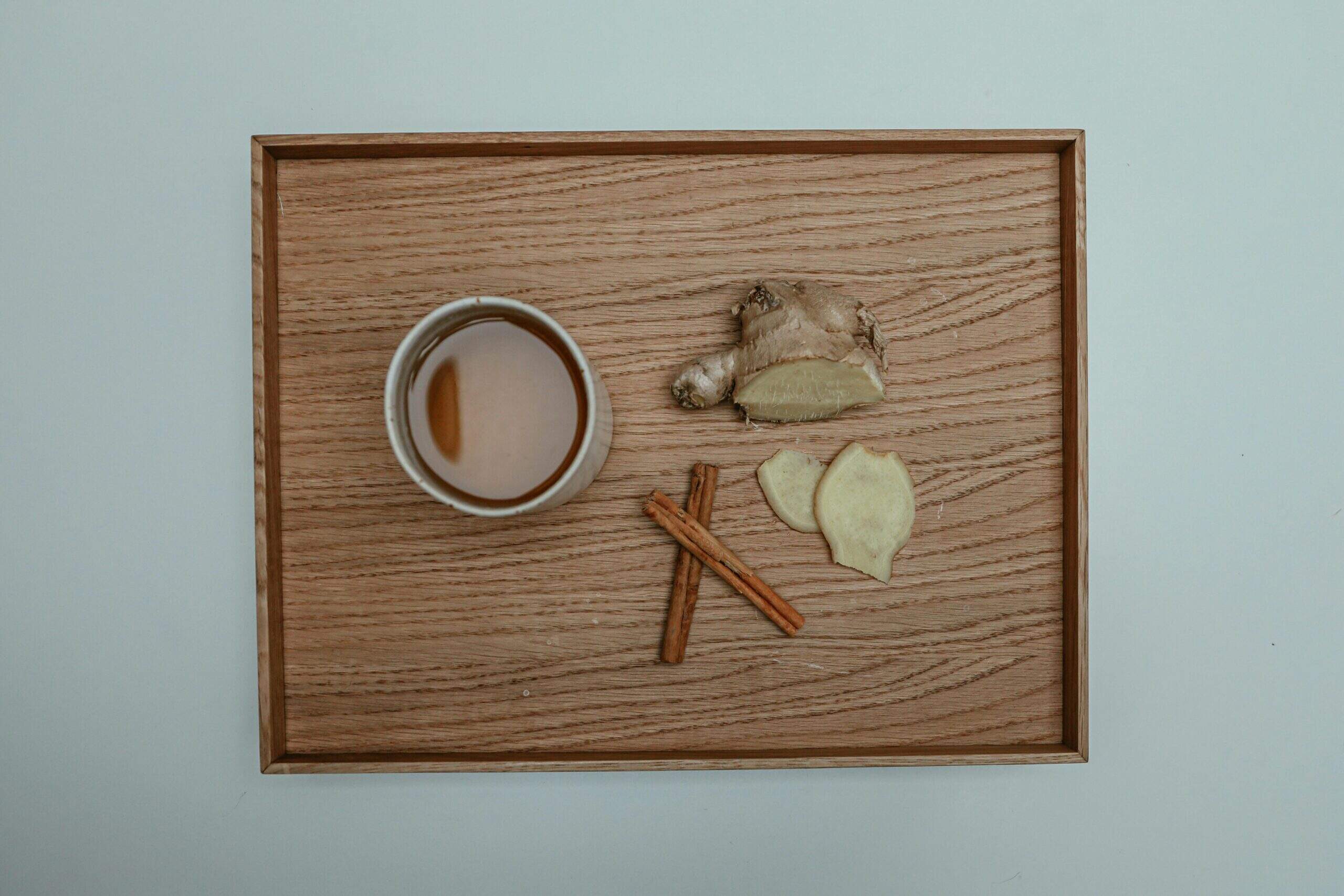 Tasse de tisane accompagnée de gingembre frais et de bâtons de cannelle sur un plateau en bois clair