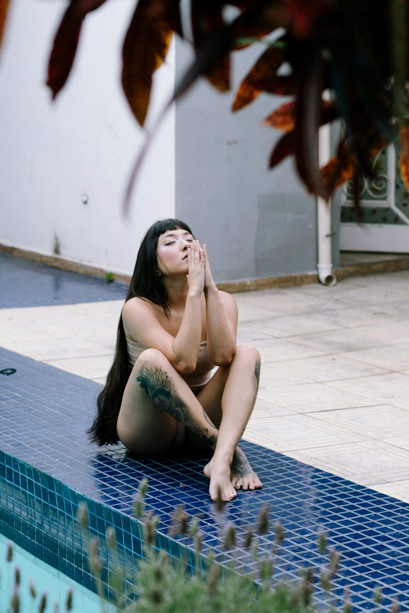 Femme assise au bord d’une piscine, les yeux fermés et les mains jointes devant le visage, en pleine séance de méditation.