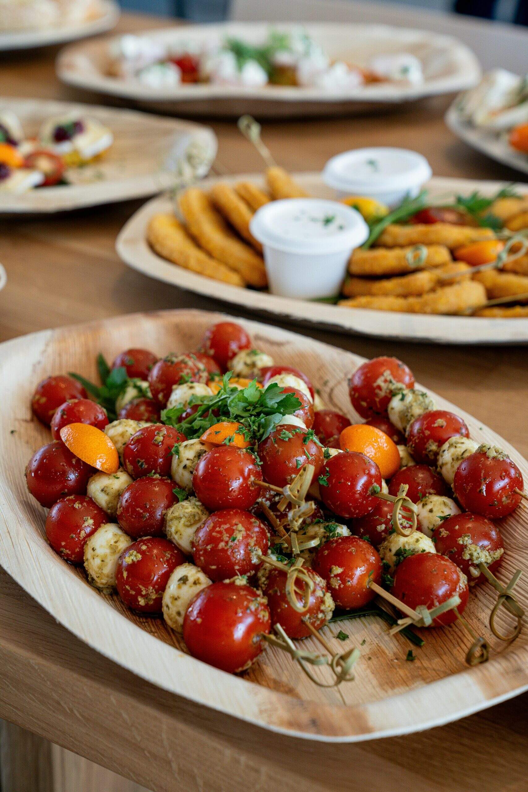 Brochettes de tomates cerises et billes de mozzarella au pesto servies dans une assiette en bois