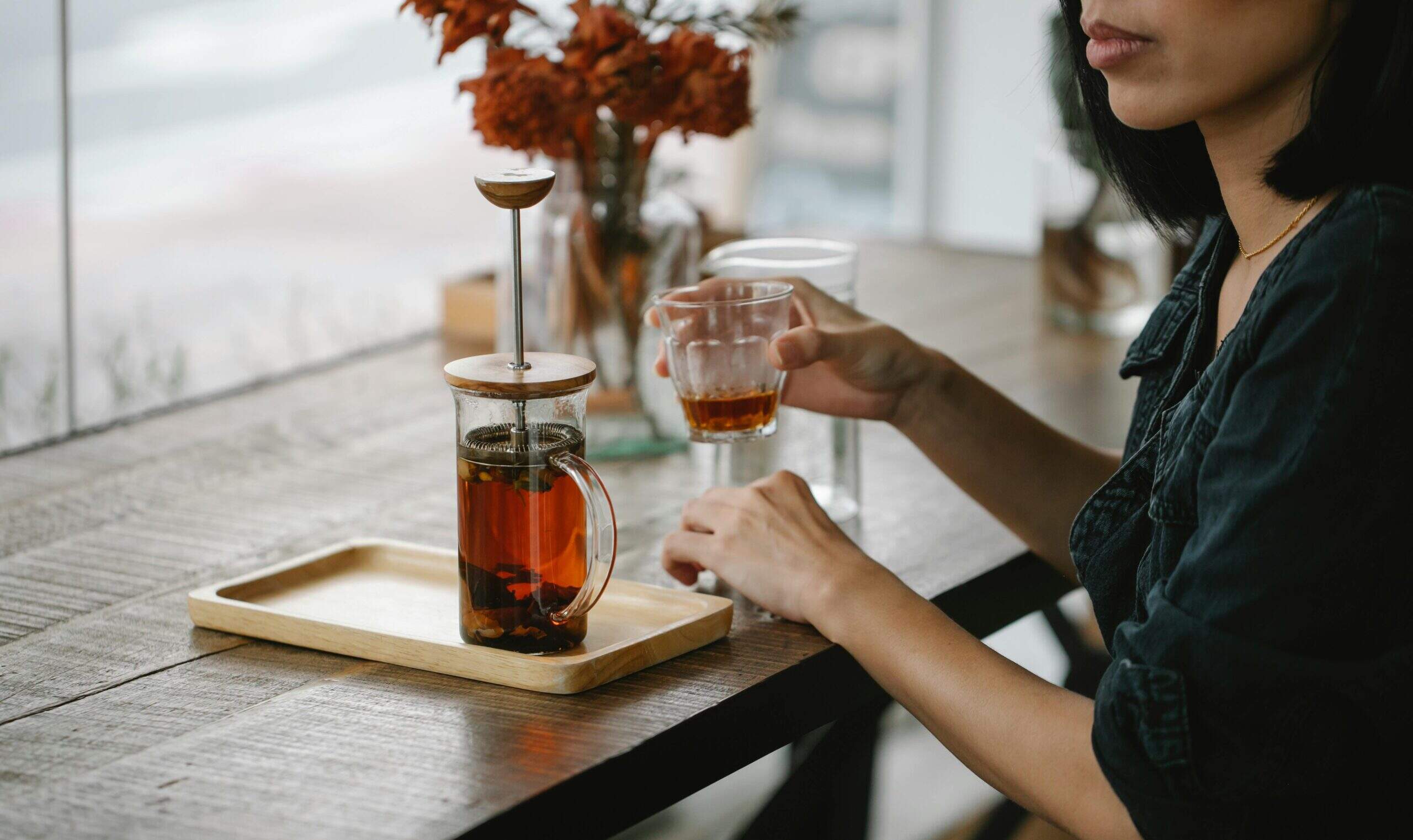 Femme assise à une table en bois, dégustant une infusion dans une cafetière à piston