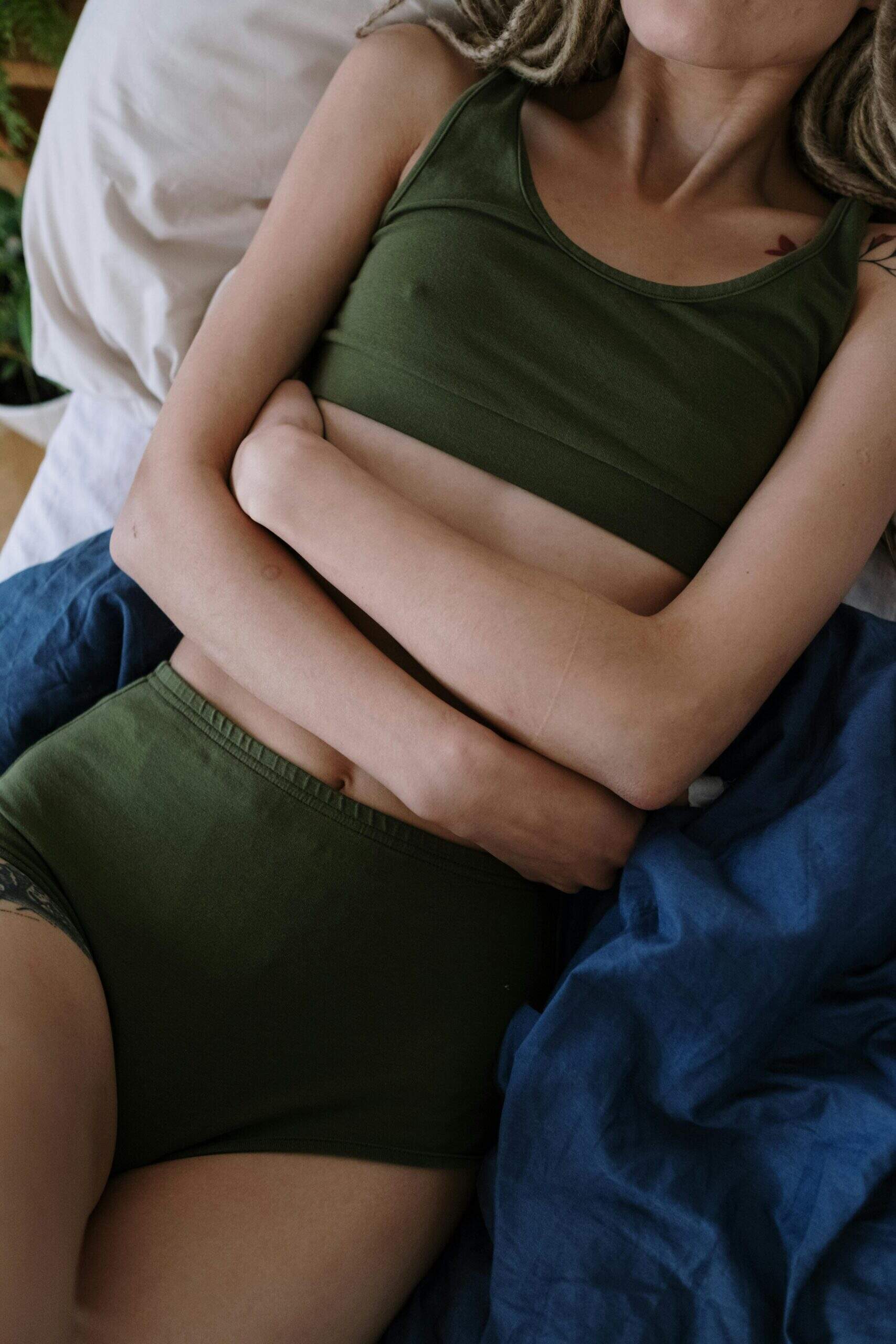 Femme allongée sur un lit, tenant son ventre, illustrant une douleur ou un inconfort abdominal