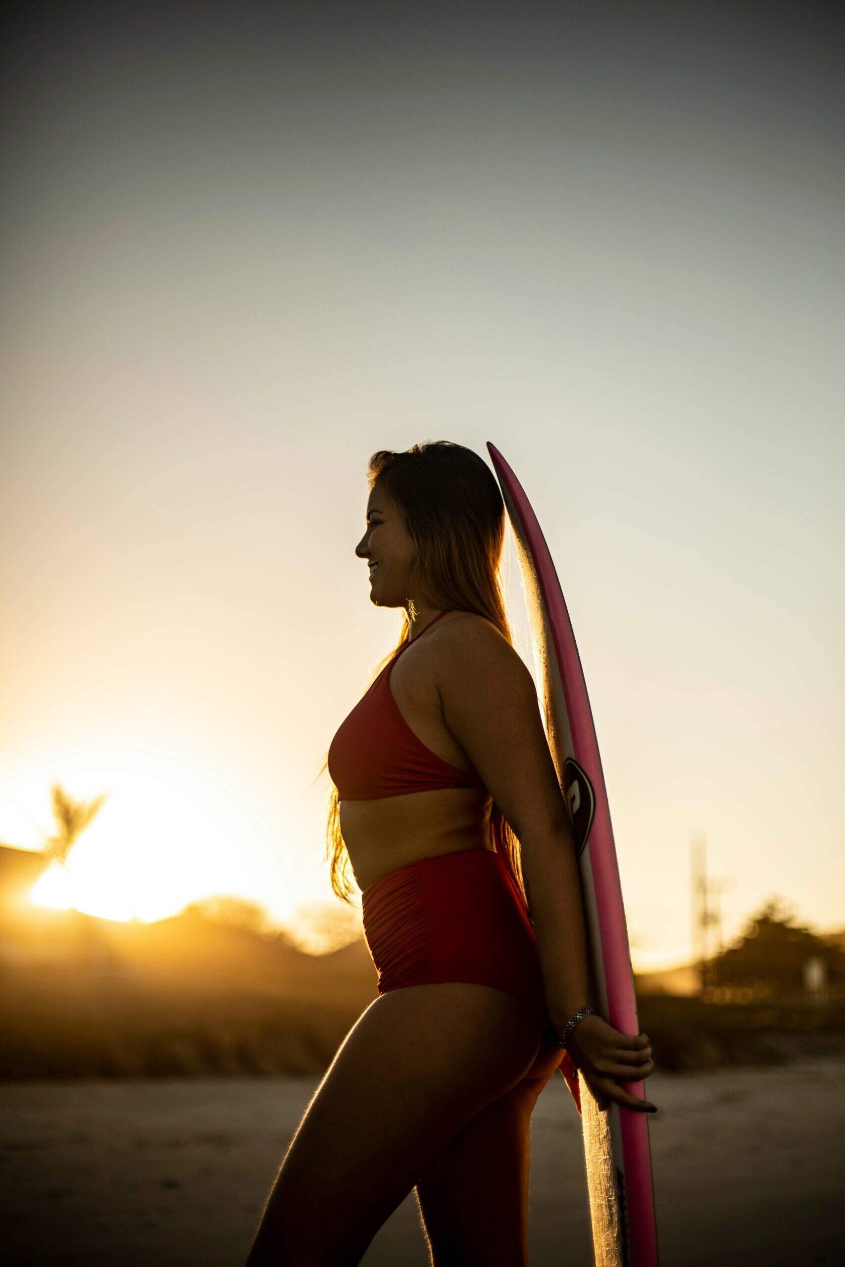 Femme en maillot de bain rouge tenant une planche de surf au coucher du soleil sur la plage