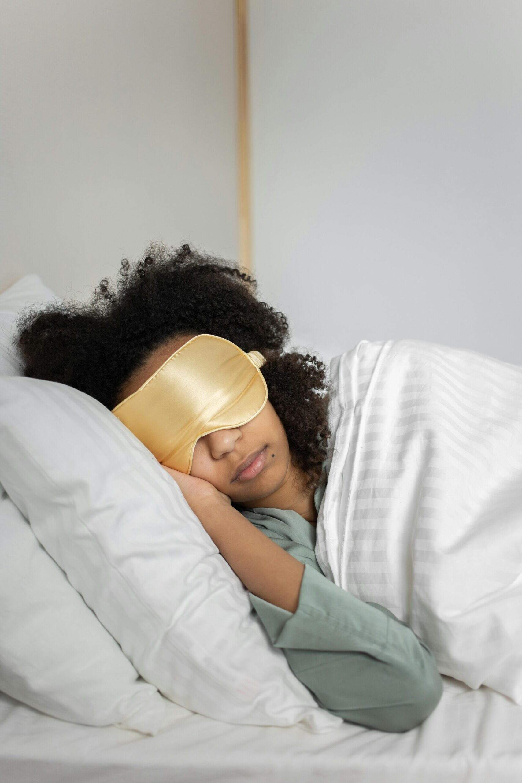 Femme dormant avec un masque de sommeil doré sur un oreiller blanc