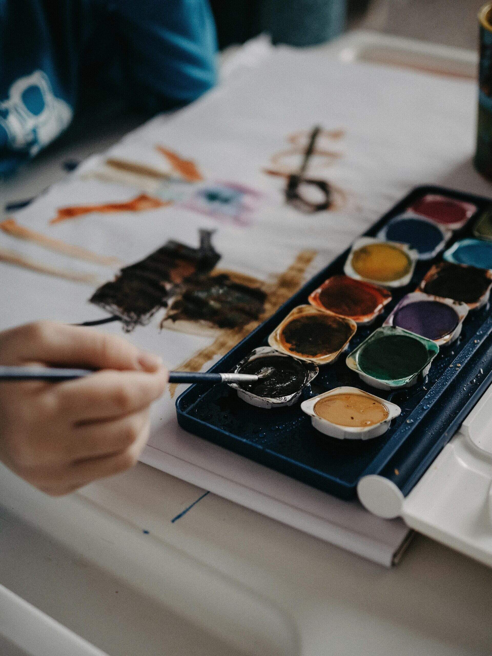 Main d'un enfant peignant avec de l’aquarelle sur une feuille blanche