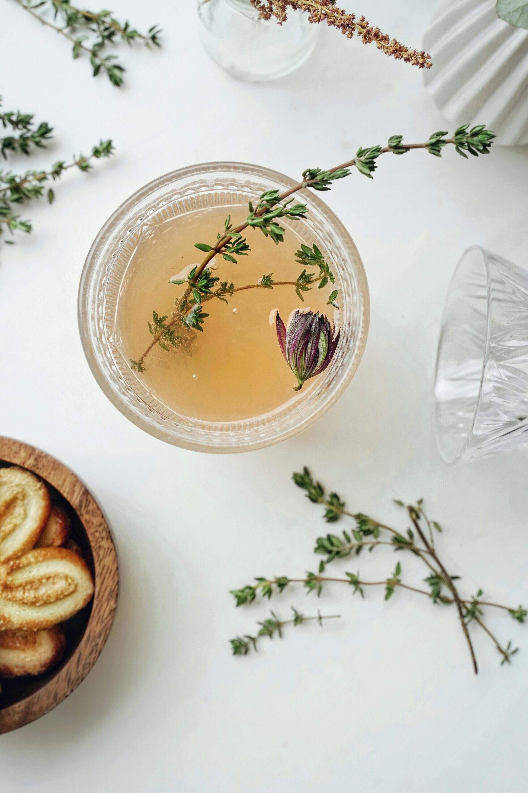 Boisson claire dans un verre avec herbes fraîches et fleur séchée, sur une table décorée de branches de thym