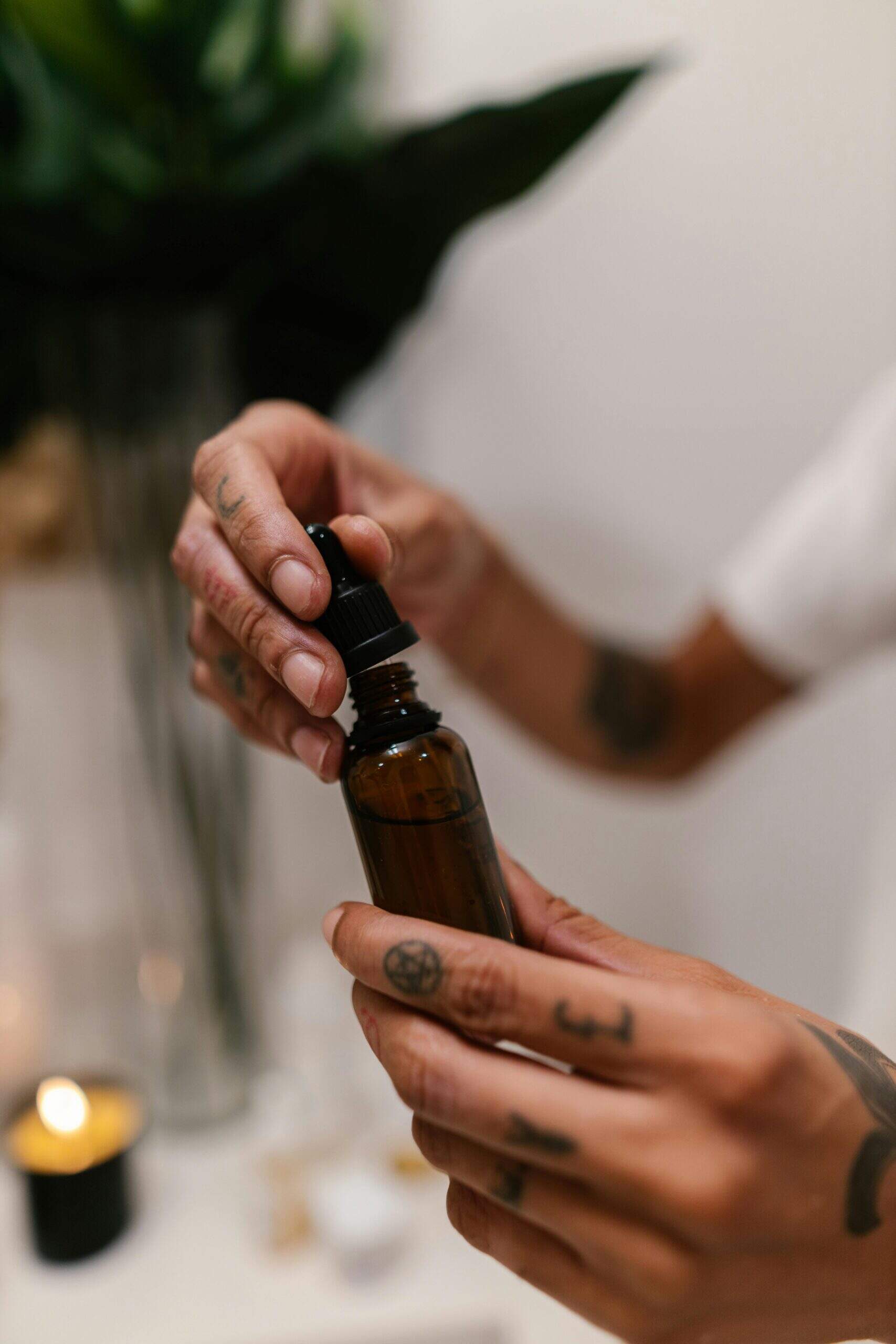 Main tatouée tenant un flacon ambré avec pipette, contenant un élixir ou une huile essentielle naturelle