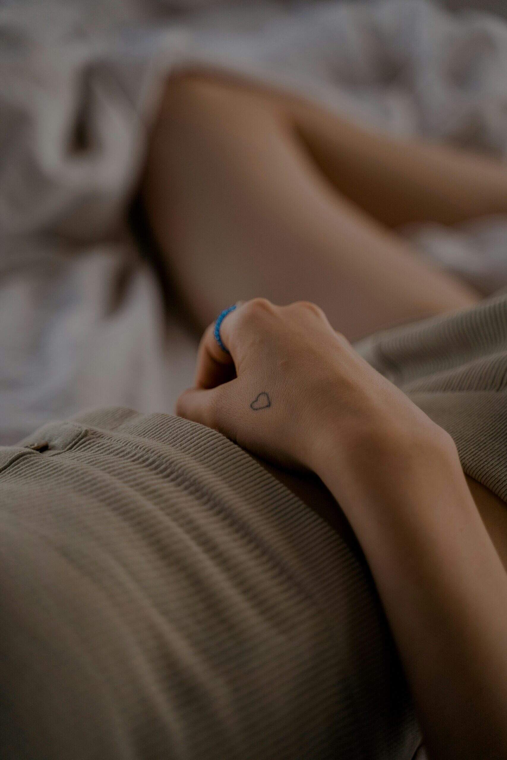 Une main avec un petit tatouage en forme de cœur repose sur un ventre vêtu d’un vêtement côtelé beige