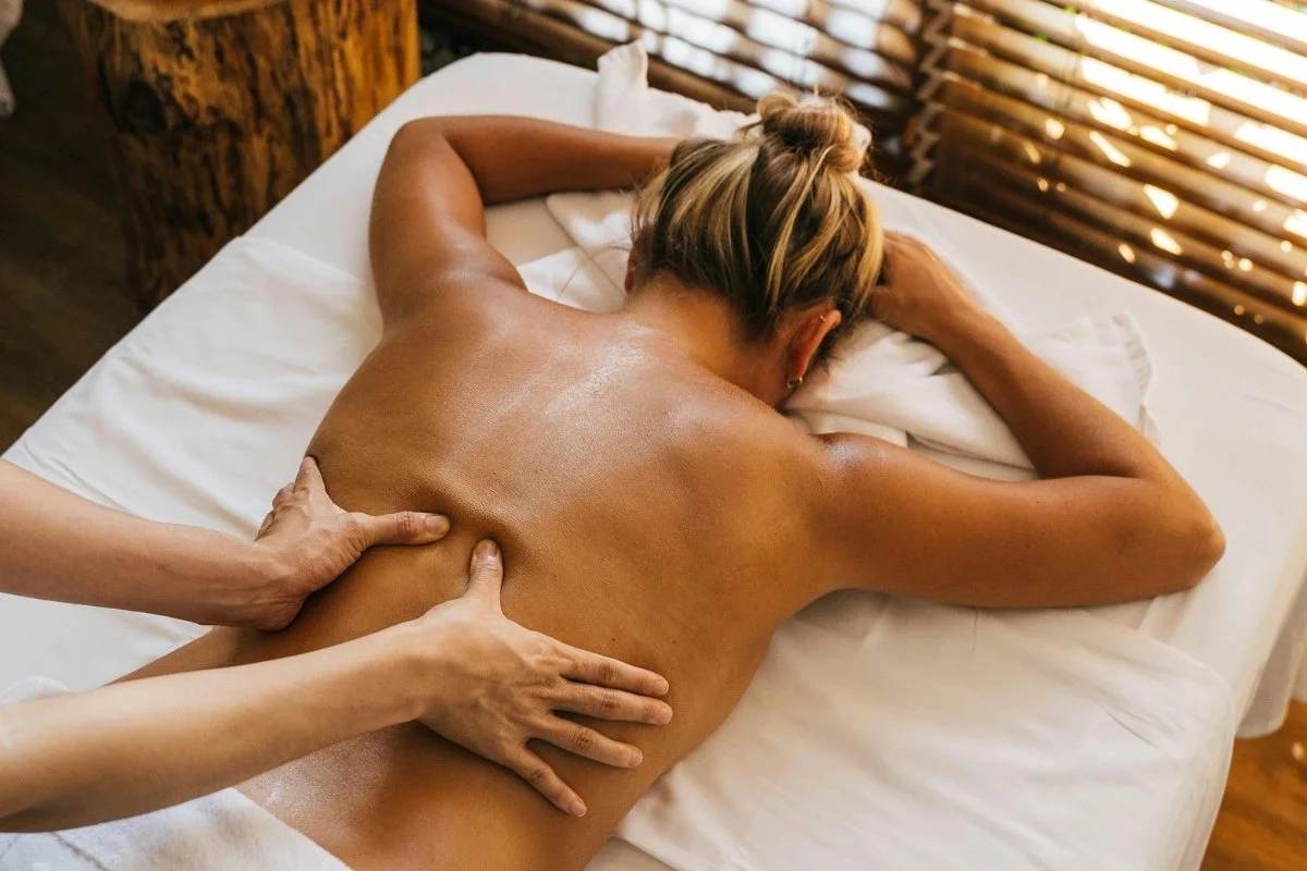 Massothérapeute qui masse une cliente sur une table de massage durant une séance.