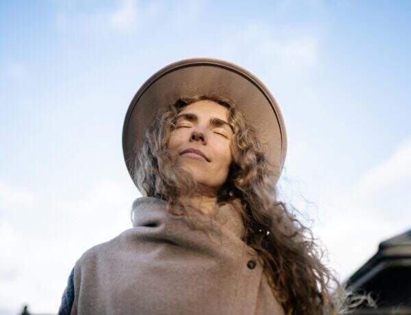 Femme aux cheveux bouclés et chapeau beige profitant du soleil les yeux fermés