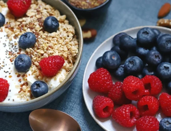 Bol de skyr avec des fruits frais, du muesli et accompagné d'une assiette de framboises et de myrtilles.