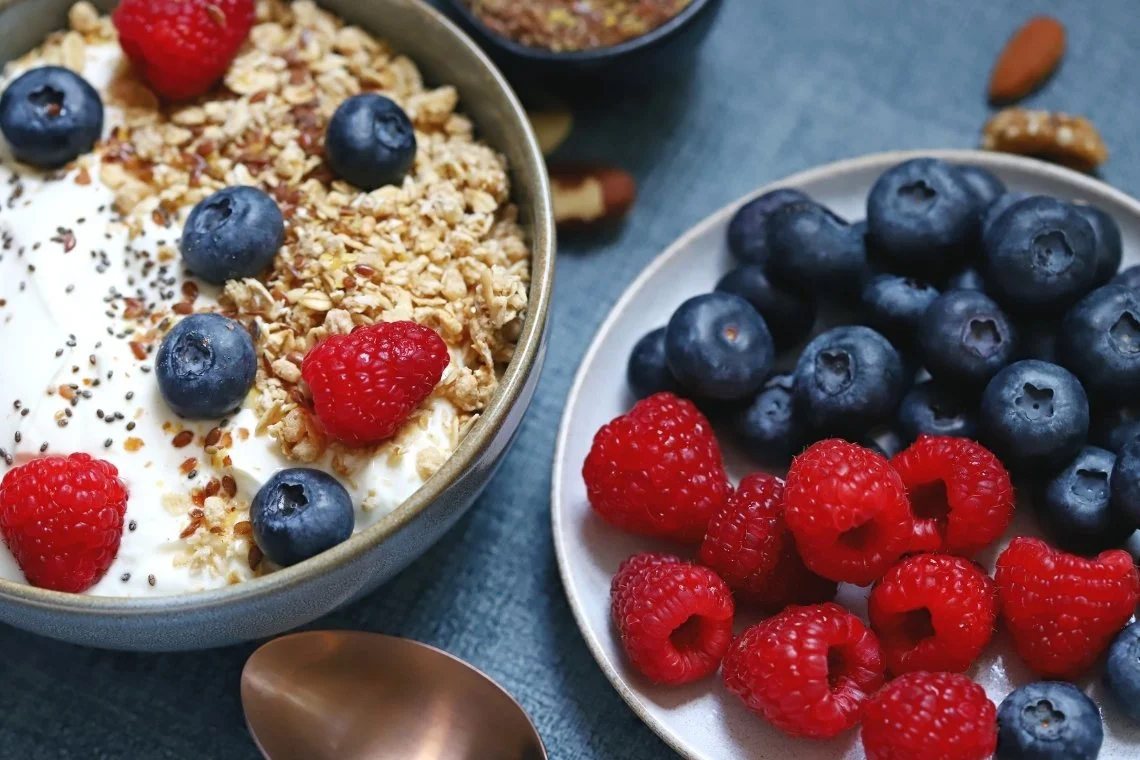 Bol de skyr avec des fruits frais, du muesli et accompagné d'une assiette de framboises et de myrtilles.