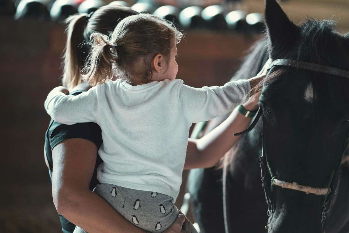 Une personne accompagnatrice avec une enfant touchant un cheval durant une séance d'équithérapie