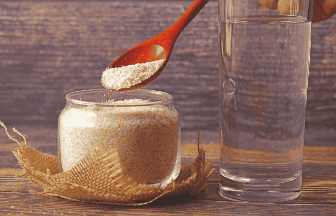 poudre de psyllium blond à côté d'un grand verre d'eau