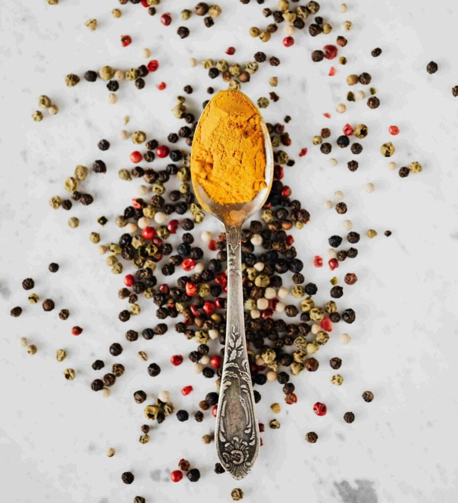 cuillère de poudre de curcuma avec grains de poivre noir