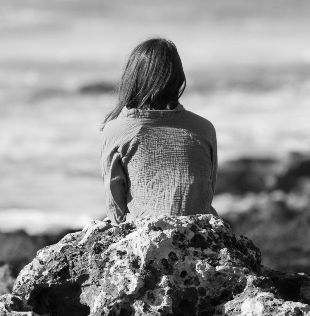 femme de dos sur un rocher réfléchissant face à la mer